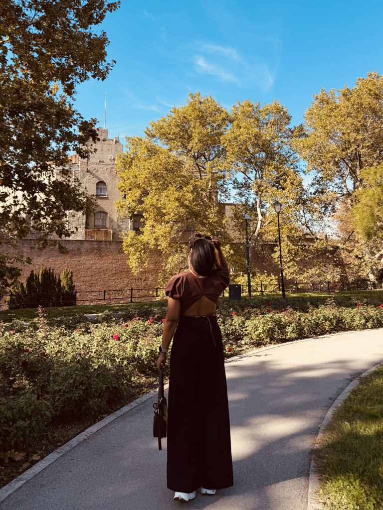 A woman walking along a path in Kalemegdan park among autumn trees and fortress walls