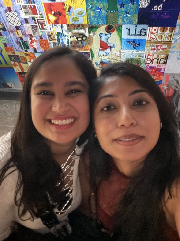 Two friends smiling in a selfie in a colourful bar after midnight