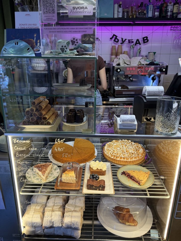 A café counter full of cakes and pastries under a neon sign
