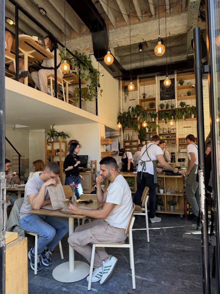 The busy, plant-filled interior of Café Bloom in Dorćol, with a mezzanine and hanging lights