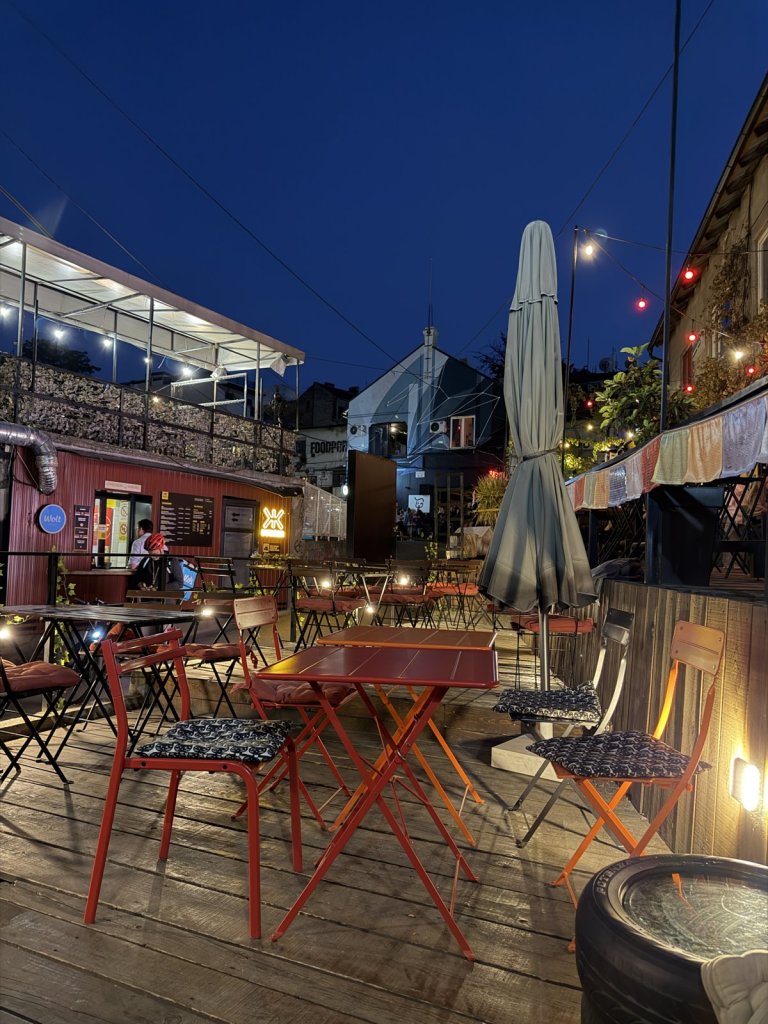 An outdoor café terrace with red chairs and string lights at dusk