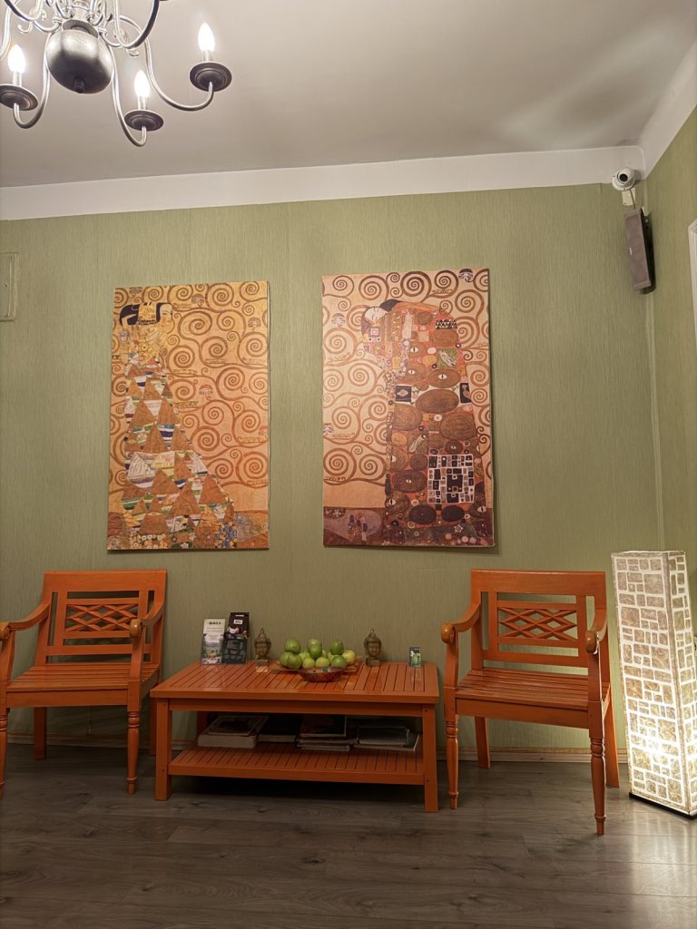 A calm massage studio waiting room with orange wooden chairs and Klimt prints